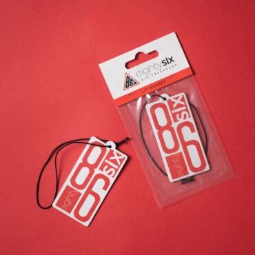 Lit Sunset Air Freshener and its respective packaging on a red backvground.